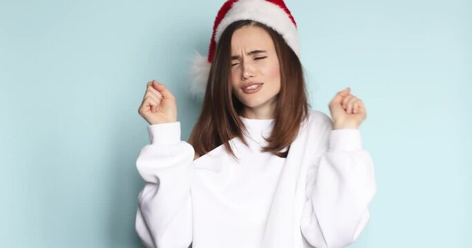Young woman in Santa Christmas hat and white sweater dancing, singing fooling around having fun expressive gesticulating hands isolated on blue background studio. Happy New Year Merry holiday concept