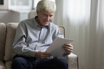 Angry stressed senior man staring at document, reading paper letter, bank notice, medical insurance agreement, feeling mad, frustrated, nervous, worried, finding money loss, mistake, error