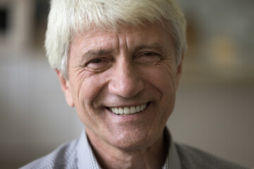 Cheerful happy old mature Caucasian man with wrinkles and gray hair close up portrait. Senior male model posing indoors, looking at camera, smiling, showing perfect white teeth