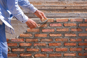 Close up of mature builder hands is making low brick fence wall for planting hedges in house construction site