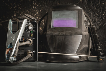 Welding helmet and welding inverter machine with electrode close up on the metal workbench...