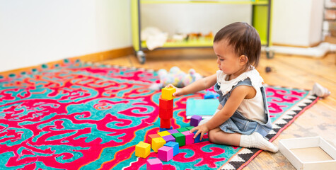 Toddler girl playing with wooden cubes in kindergarten