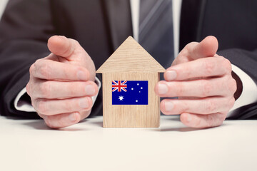 Businessman hand holding wooden home model with Australian flag. insurance and property concepts