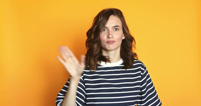 Be quiet. Attractive playful woman uses sign language zips mouth with hands asks to keep secret has mysterious happy look poses against yellow background.