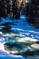 Baker Creek flowing past snow covered banks. Banff National Park, Alberta, Canada