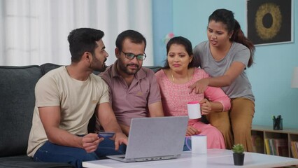 Indian parents with siblings making online payment for shopping by using credit card on laptop at home - concept of secure banking, financial transaction and family togetherness. - Powered by Adobe