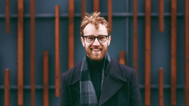 A young red-haired guy, a businessman in glasses, looks at the camera against the background of an urban style. Close up portrait