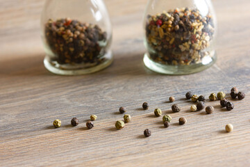 Peas of multi-colored peppers and glass pepper shakers are scattered on a wooden table.