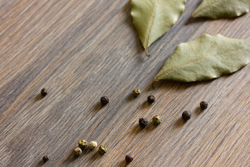 Peppercorns and bay leaves are scattered on a wooden table.