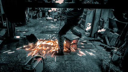 A man welds the bottom of a car. Sparks from welding under the feet of the welder. Car repair in the garage