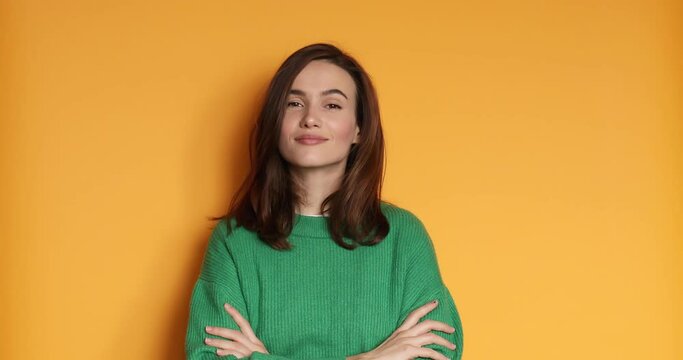 Happy woman in green sweater crosses arms on chest in the studio, yellow background. Woman smiles and proud of herself.