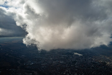 Aerial view from airplane window at high altitude of distant city covered with white puffy cumulus...