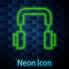 Glowing neon line Headphones icon isolated on brick wall background. Earphones. Concept for listening to music, service, communication and operator. Vector