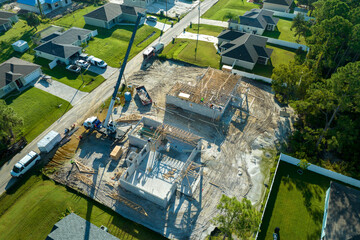 Lifting crane truck and builders working on roof construction of unfinished residential house with...