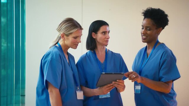 Team of three mature female doctors wearing scrubs meeting and checking digital tablet in hospital - shot in slow motion