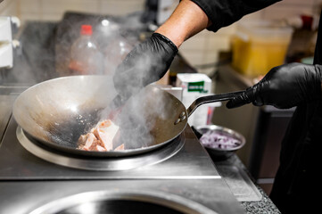 Professional chef cooking chicken food in wok pan on kitchen