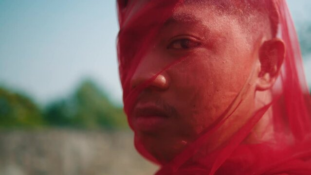 the face of an Asian man wrapped in a red scarf with an angry expression