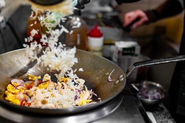 Chef cooking stir fry rice and chicken in wok pan at restaurant kitchen.