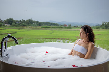 Large open-air round bath, woman takes bubble bath and enjoys beautiful view of the forest, relaxation time concept, copy space