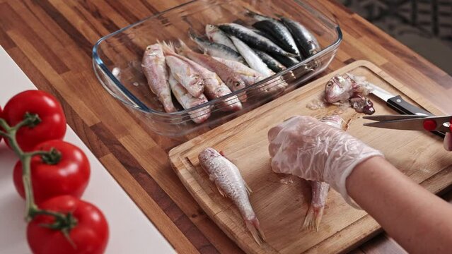 Close-up view of housewife hands cleaning fish on a wooden cutting board. Cooking red mullet fish, real time