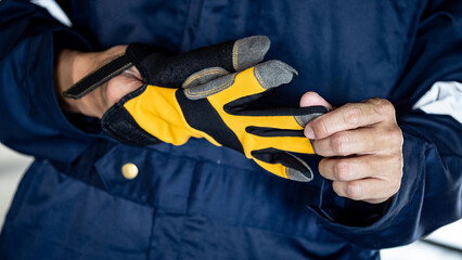 Male auto mechanic taking off yellow gloves from his hand. Protective workwear for car repairing service and maintenance