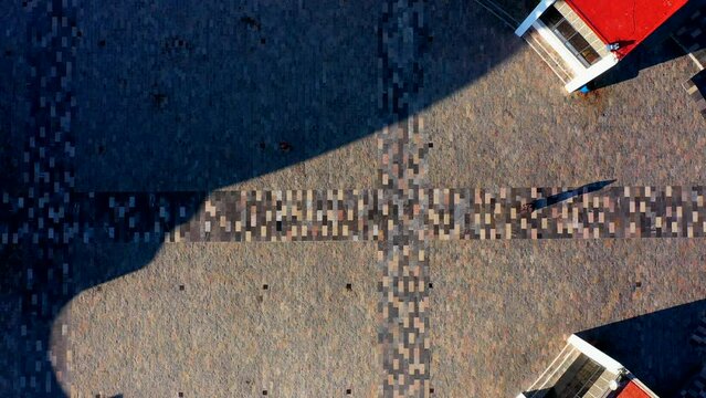 Persona silueta caminando sobre mosaicos de texturas en el piso en el camino en la calle proyectando una sombra sobre la explanada en un d&iacute;a soleado en la vereda con piedras paisaje sombreado 