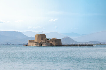 Fototapeta na wymiar Bourtzi Fortress on a small island in Nafplio surrounded by water with mountains in the background, viewed from the port