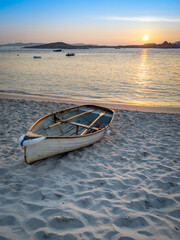 White rowing boat on a fine white sandy beach at sunset.