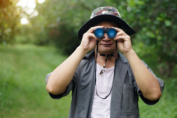 Asian man ecologist use binocular to survey nature in forest. Concept, nature exploration. Ecology...