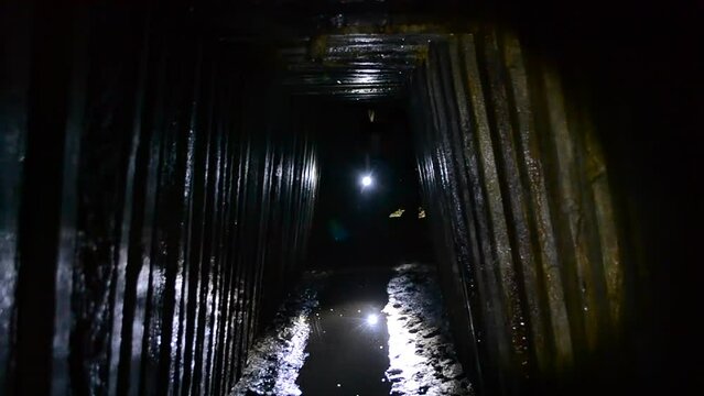 Digger person walking through dark tunnel adit, rain collector, sewer tunnel underground, illuminating light of lantern flashlight. Infrastructure of mine adit for underground river. Sewage collector