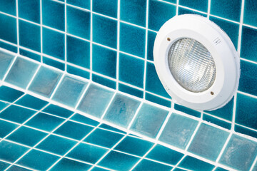 White LED light in a swimming pool without water on a turquoise tile wall pattern. Waterproof lighting fixture in swimming pool