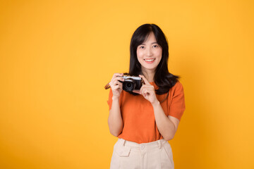 Young asian woman with a camera, ready for a fun adventure tour. Positive holiday vibes on a yellow background