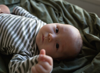 mixed race newborn baby lies wrapped in a green muslin swaddle