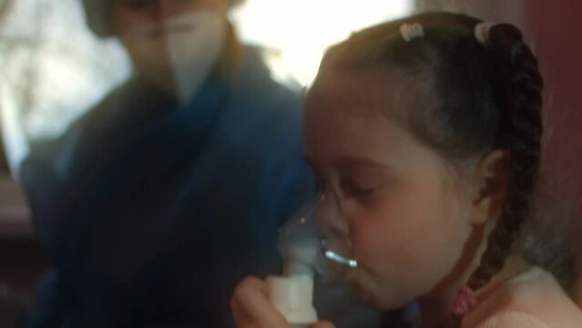 Beautiful little girl makes inhalation using a compressor inhaler at hospital. 5 y.o. girl inhaling saline vapors with nebulizer mask on her face. Doctor helps little girl make inhalation at hospital