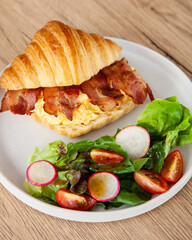 Croissant with scrambled egg, bacon and salad