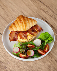 Croissant with scrambled egg, bacon and salad
