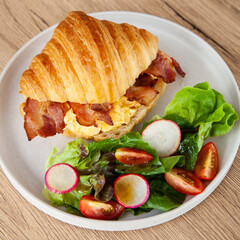 Croissant with scrambled egg, bacon and salad