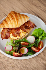 Croissant with scrambled egg, bacon and salad