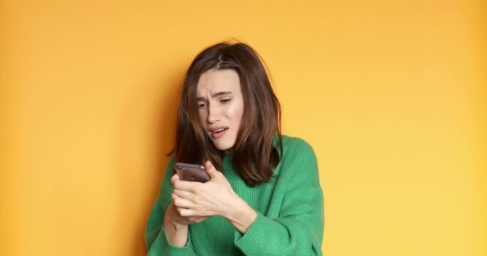 Unhappy woman in green sweater feeling annoyed holding crashed smart phone. Broken by the phone. Woman in shock with a broken smartphone. Screen broken and damaged.