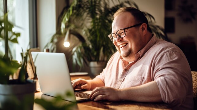 touching image of a young man with Down Syndrome sitting at his cozy home desk and using a laptop computer with a sincere smile.