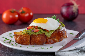 Challah Avocado Toast with diced tomato and a sunny side up egg on top.