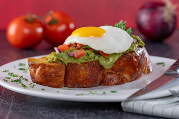 Challah Avocado Toast with diced tomato and a sunny side up egg on top.
