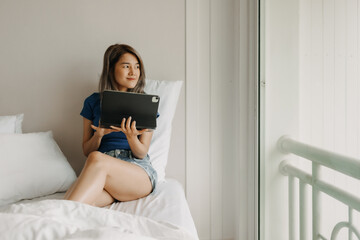 Happy freelance asian woman work on tablet on the hotel bed on travel trip.