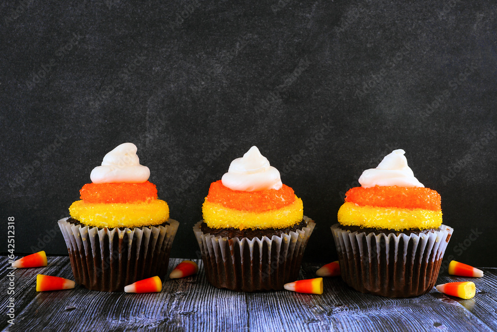 Poster halloween candy corn chocolate cupcakes in a row against a dark background