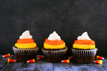 Halloween candy corn chocolate cupcakes in a row against a dark background