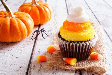 Halloween candy corn chocolate cupcake. Close up against a white wood background.