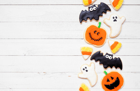 Halloween cookie side border. Overhead view on a white wood background with copy space. Ghosts, bats, jack o lanterns and candy corn.