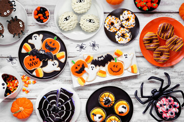 Spooky Halloween dessert table scene over a white wood background. Top view. Collection of cookies, cakes, donuts and candies.