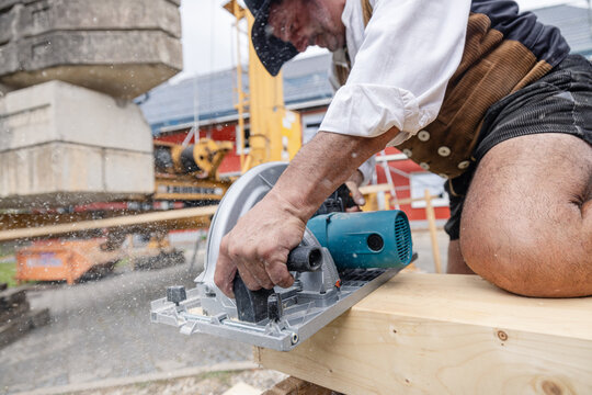 carpenter on a construction site cutting a wooden beam with an electrical saw