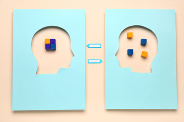 Cubes visible through cut blue papers in shape of human heads on beige background. Logic concept